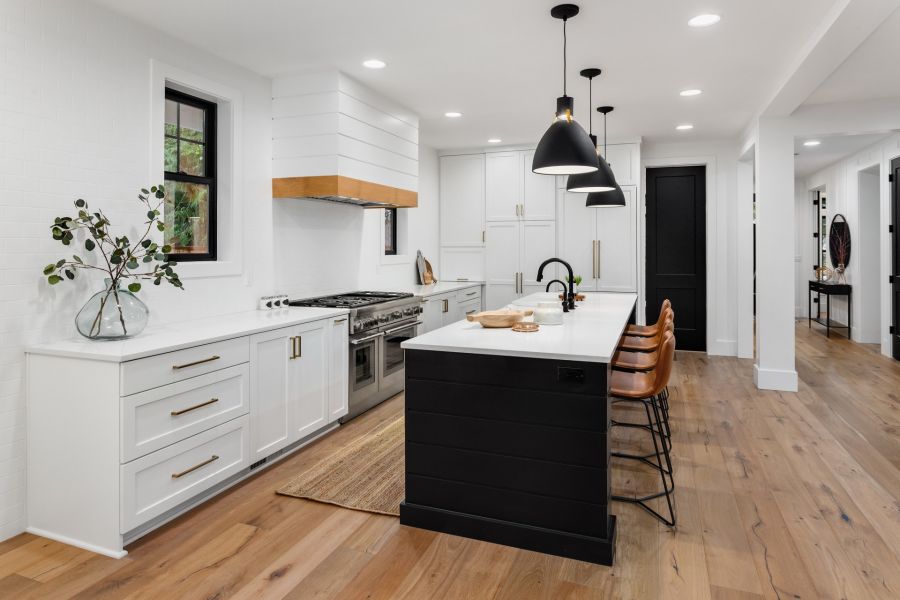 Modern white kitchen with black island, pendant lights, and wood flooring in a remodeled home